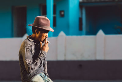 Young man smoking cigarette against wall