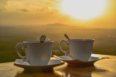 Coffee cup on table against sky during sunset