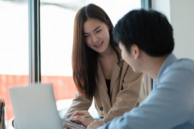 Young woman using laptop with colleague at office