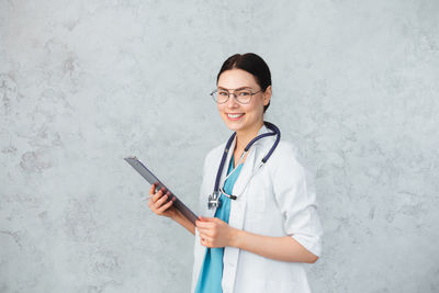 Portrait of smiling young woman standing against wall