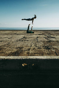 Full length of man balancing woman against clear sky