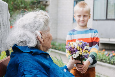 Volunteer boy and senior elderly woman with gift, flowers bouquet and basket of groceries