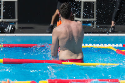 Rear view of shirtless man swimming in pool