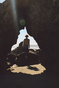 Rear view of woman standing on rock formation at beach