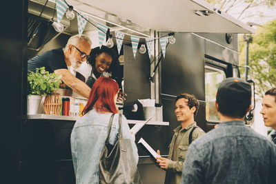 Owner with assistant talking to smiling customers by food truck