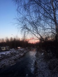 Bare trees by river against sky during winter