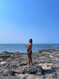 Full length of woman standing at beach against clear blue sky