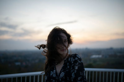 Portrait of woman standing by railing against sky during sunset