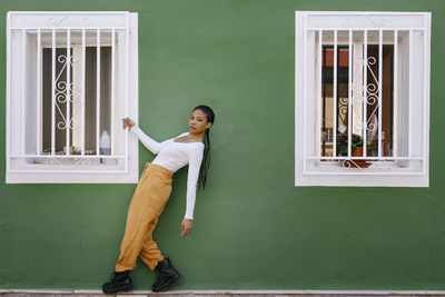 Young woman holding window grate by green wall outside house