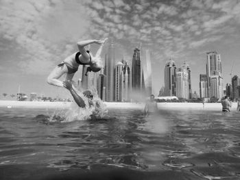 Woman backflipping from shoulder of man in sea against sky