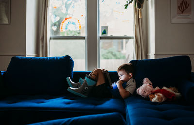 Preschool age boy laying on couch watching tablet on rainy day