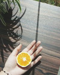 Cropped hand of woman holding orange slice on table