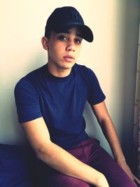 Portrait of teenage boy sitting on bed against wall at home