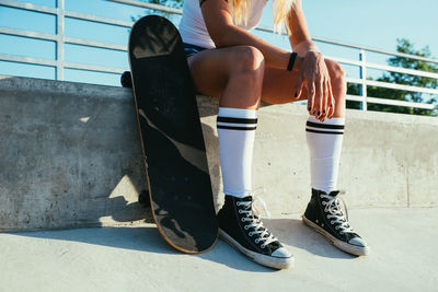 Low section of woman sitting by skateboard on floor
