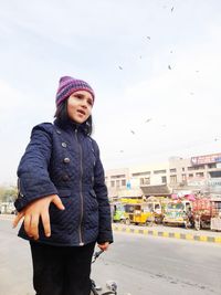 Portrait of young woman standing against city