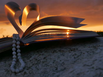 Close-up of heart shape made of pages against sky during sunset