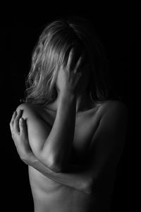Shirtless woman covering face against black background