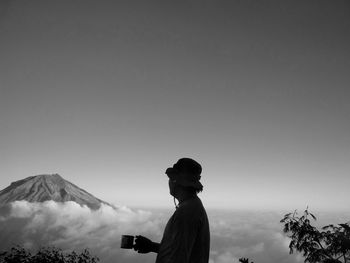 Side view of man standing on mountain against clear sky