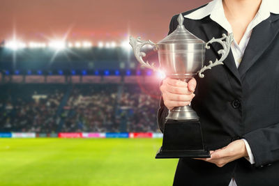 Midsection of businesswoman holding trophy at stadium