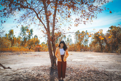 Portrait of young woman standing by tree during autumn