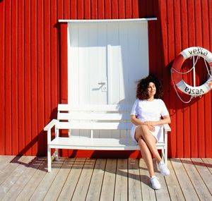 Woman sitting on bench against red wall