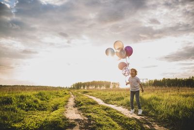 Full length of boy standing on field against sky whith balloons