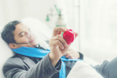 Ill man holding heart shape prop while lying on bed at hospital
