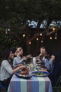 Side view of happy friends having dinner at table in yard