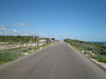 Road leading towards city against blue sky