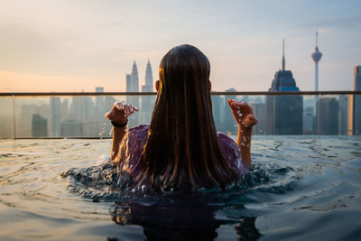 Rear view of woman in infinity pool against buildings in city