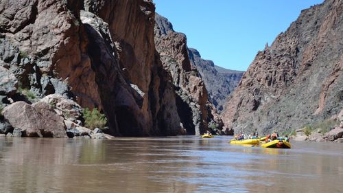 People in inflatable raft on river amidst rocky mountains