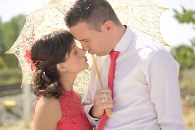 Young couple rubbing noses while holding umbrella on sunny day