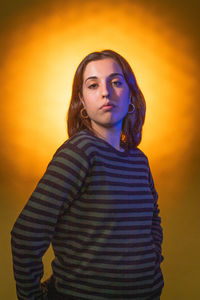 Portrait of young woman standing against yellow background