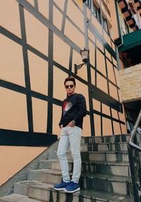 Full length of fashionable man standing on steps against wall