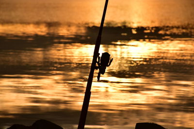 Silhouette fishing rod on sea against sky during sunset