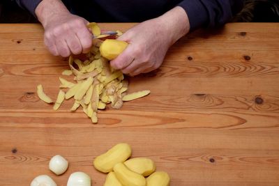 Cropped hands of man peeling potatoes on table