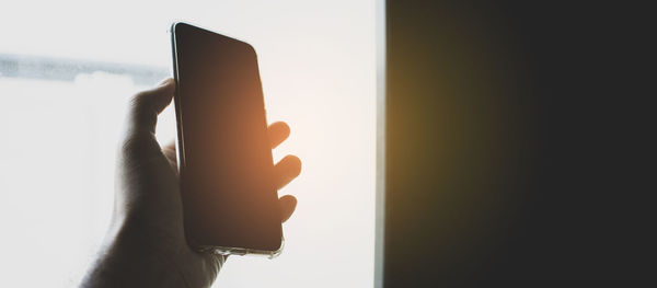 Close-up of hand holding mobile phone against window