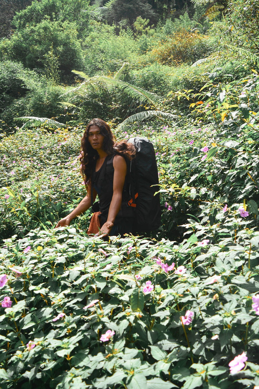 YOUNG WOMAN SITTING ON FLOWERING PLANTS