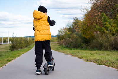 Boy rides an electric scooter in autumn park. schoolboy using e-scooter at sunny day.