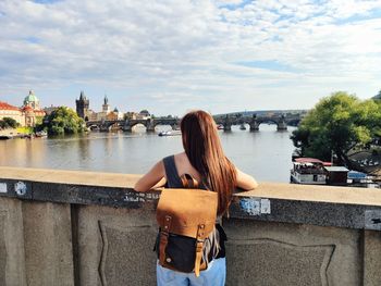 Rear view of woman by river against sky in city