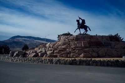 Statue by empty road against sky