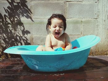 Cheerful shirtless baby girl sitting in bathtub