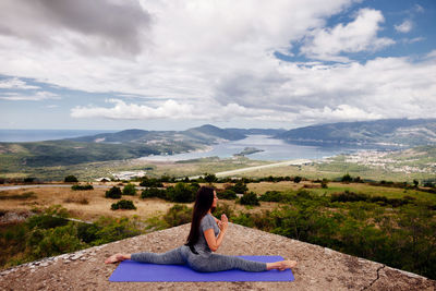 Woman practicing yoga against cloudy sky