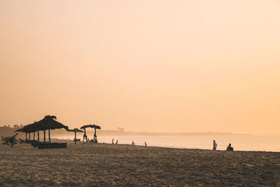 Silhouette people on beach against clear sky during sunset