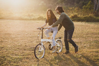 Girlfriend riding bicycle by boyfriend on land during sunset