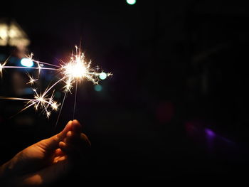 Hand holding illuminated firework display at night