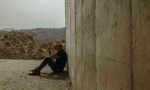 Portrait of adult man in cowboy hat sitting on ground in entrance of tunnel