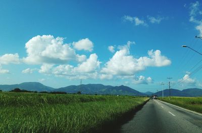 Road amidst grassy landscape against blue sky