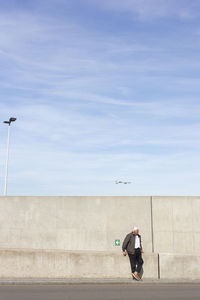 Woman walking on concrete wall against sky