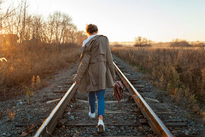 Fashion lifestyle portrait of young trendy woman dressed in brown coat, white shirt and jeans posing